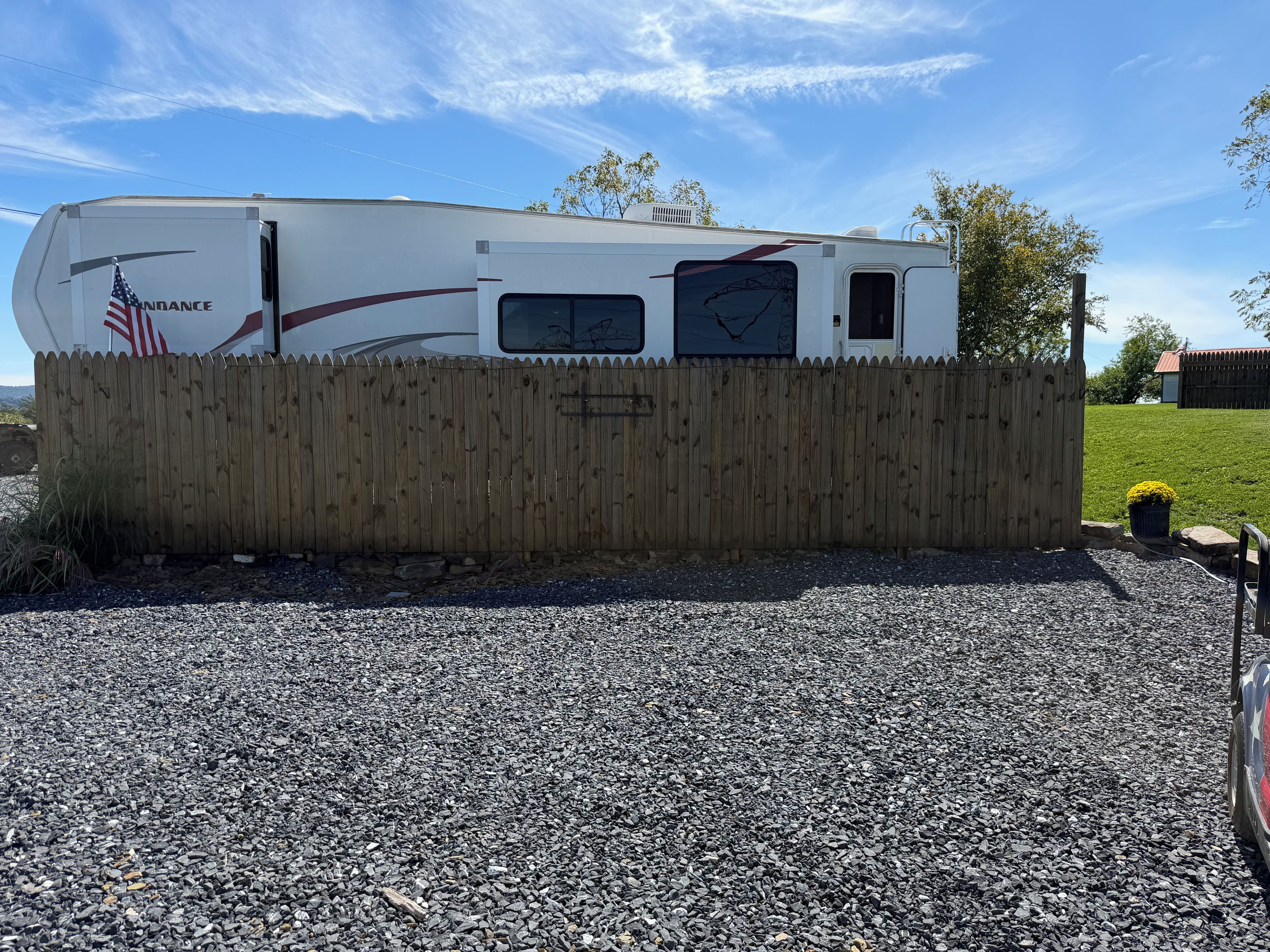 A recreational vehicle (RV) parked on a gravel surface, surrounded by a wooden fence.