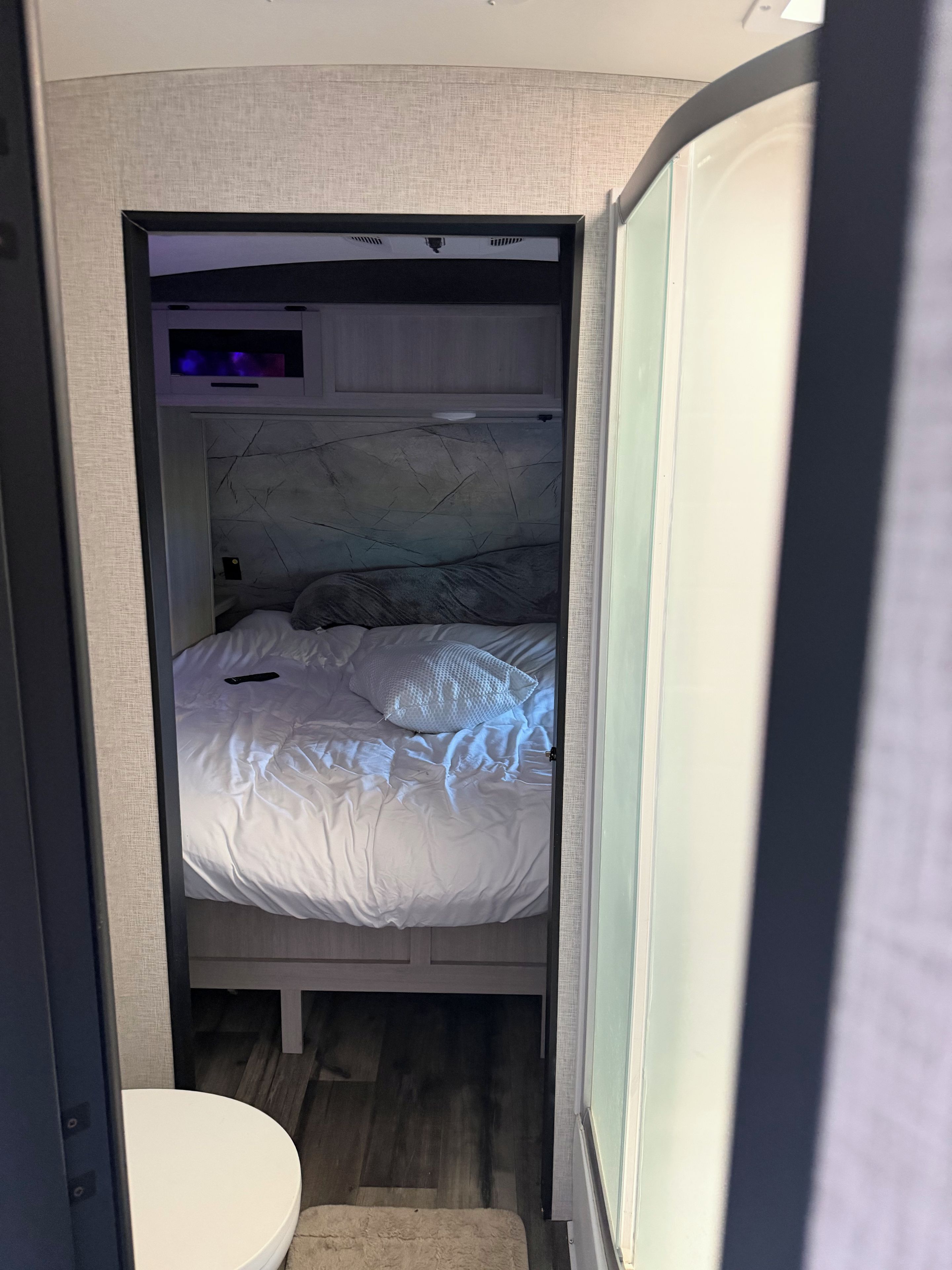 Een compacte slaapkamer met een bed, een klein nachtkastje en een ingebouwde televisie.