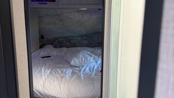 Een compacte slaapkamer met een bed, een klein nachtkastje en een ingebouwde televisie.