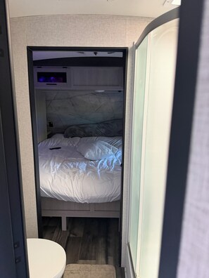 A compact bedroom with a bed, a small bedside table, and a built-in TV.