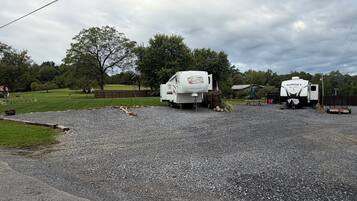 Twee campers staan op een grindpad, met een gazon en bomen op de achtergrond.