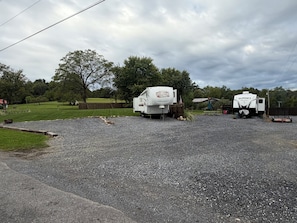 Two RVs parked on a gravel surface with a grassy area and trees in the background. - Perfect campground for a relaxing outdoor escape in Huntingdon. (Huntingdon)