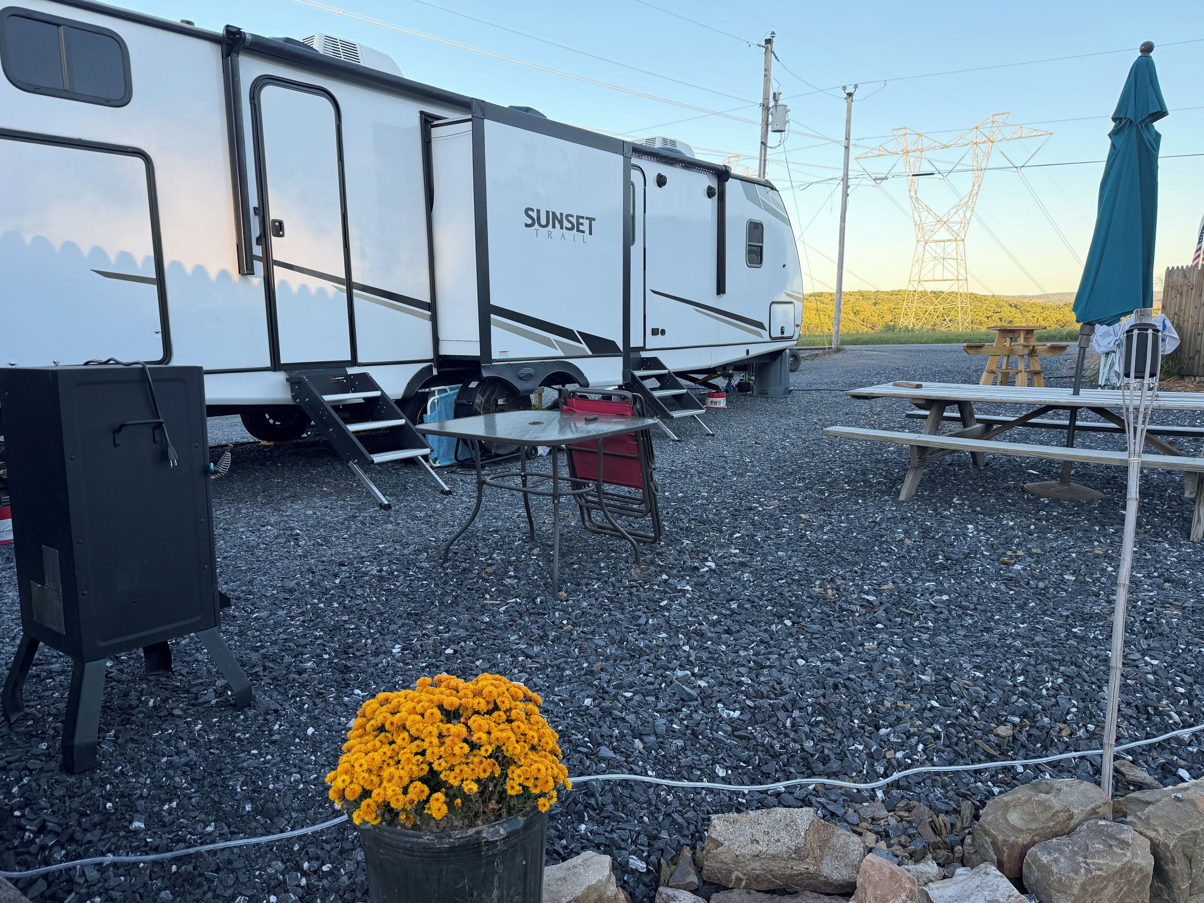 Een witte RV met 'SUNSET TRAIL' op de zijkant, geparkeerd op een grindpad.