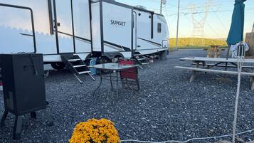 Een witte RV met 'SUNSET TRAIL' op de zijkant, geparkeerd op een grindpad.
