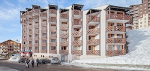 A multi-story hotel with balconies, a ski slope to the right, and a parking area with cars. - Wifi, 10m from ski slopes, ski locker, 35m², Val Thorens (Val Thorens)