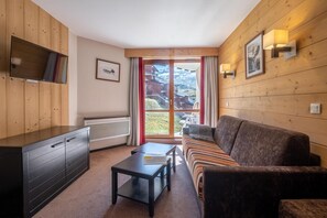 A cozy room with a sofa, a coffee table, a TV on a wooden cabinet, and a window with a view of a mountain landscape. - Wifi, 10m from ski slopes, ski locker, 35m², Val Thorens (Val Thorens)