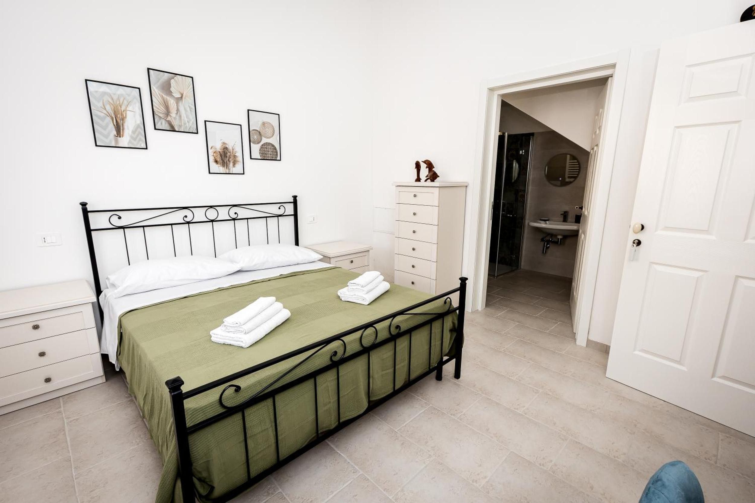 Quarto com cama, cômoda e banheiro visível por uma porta aberta.
