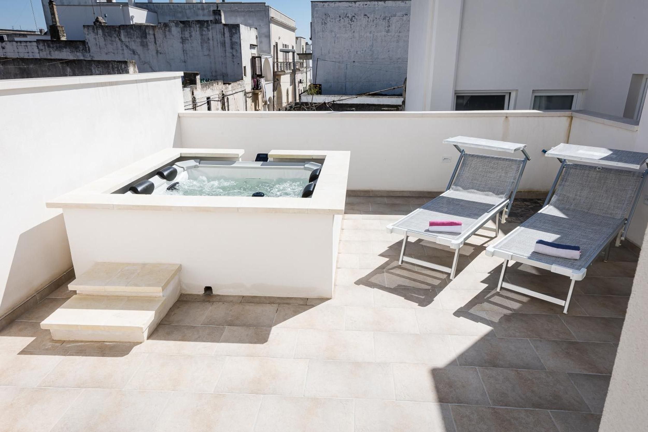 A rooftop terrace with a hot tub, lounge chairs, and a small set of steps leading to the hot tub.