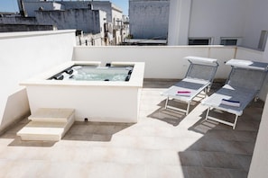 Una terraza en la azotea con un jacuzzi, sillones de descanso y unos pocos escalones que dan al jacuzzi.