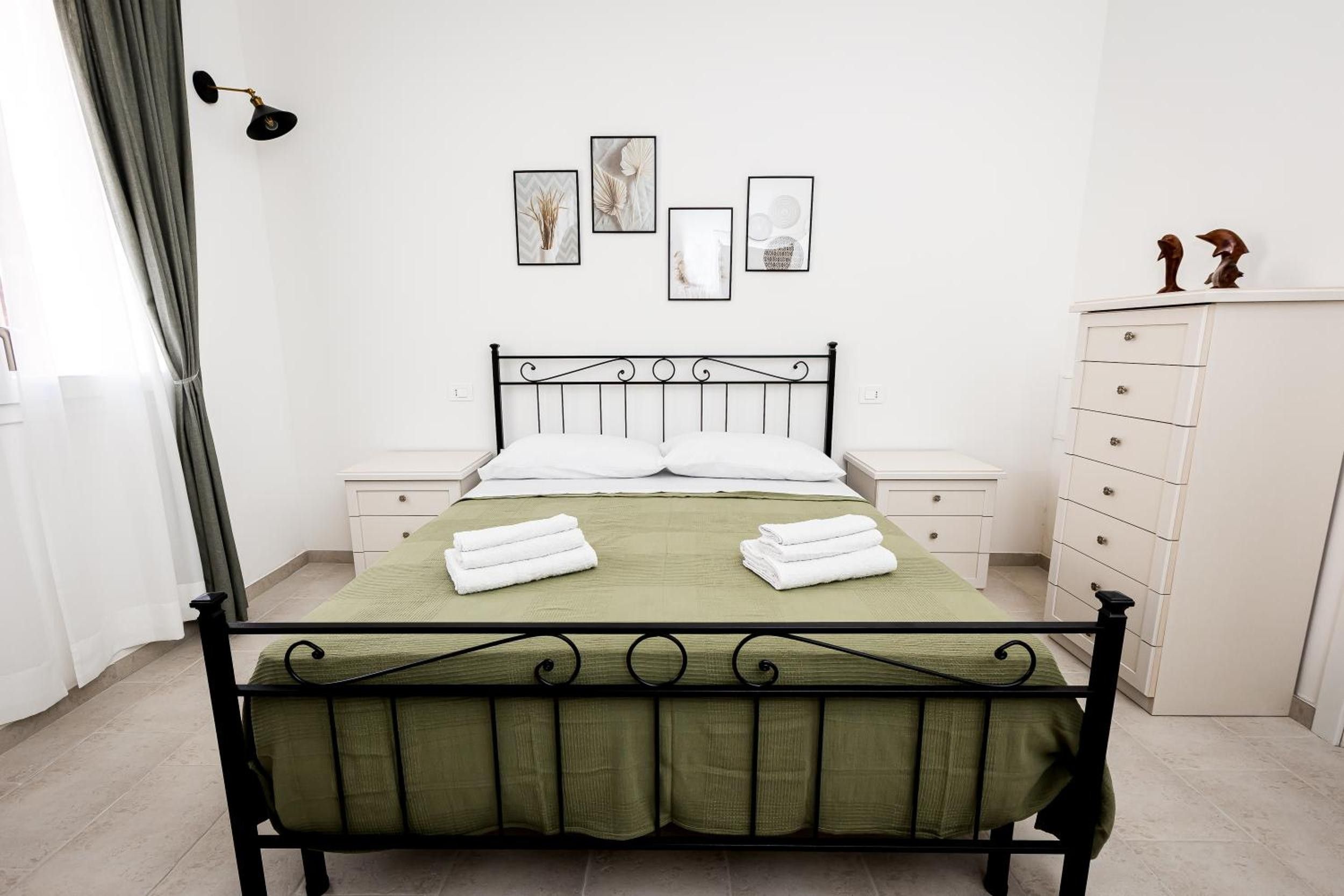 A neatly arranged bedroom with a metal bed frame, a green bedspread, white pillows, and two nightstands with white drawers.