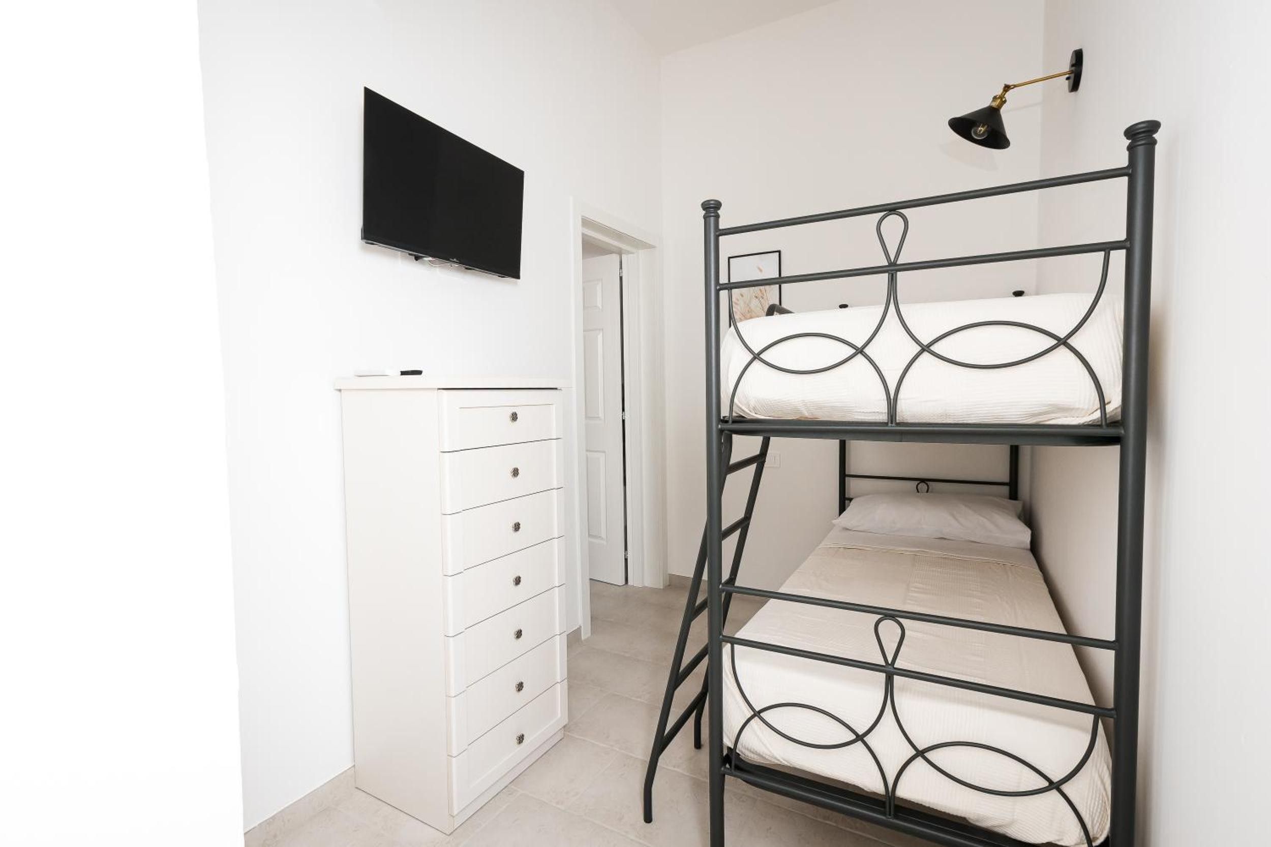 Una cama litera con un televisor encima, un aparador blanco y una puerta al fondo.