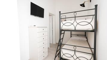 Una cama litera con un televisor encima, un aparador blanco y una puerta al fondo.