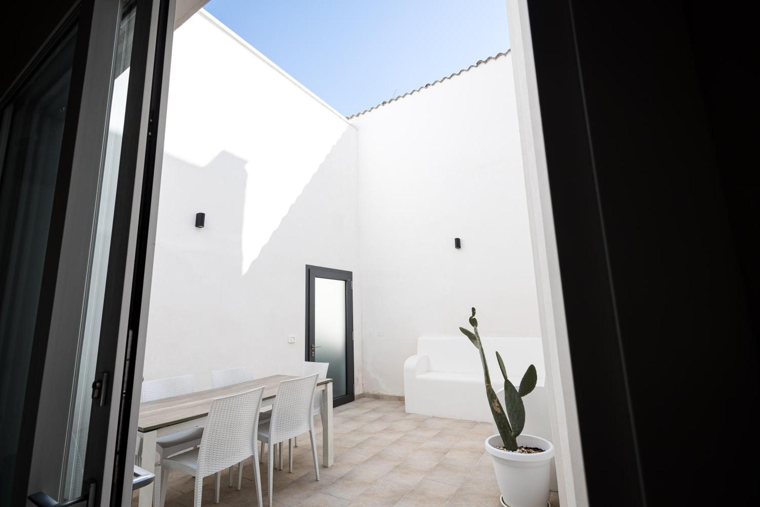 Una habitación con paredes blancas, una puerta, una mesa con sillas y una planta en maceta.