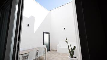 Una habitación con paredes blancas, una puerta, una mesa con sillas y una planta en maceta.
