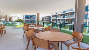 Un espacio moderno para comer al aire libre con mesas y sillas de madera redondas, con vistas a una piscina y un jardín ajardinado.