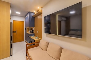 A compact room with a bed, a TV mounted on the wall, a kitchenette area, and a door leading to another room. - Makia Beach #b121 Comfort and Leisure by Carpediem (Ipojuca)