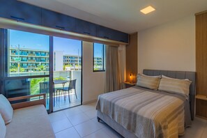 A modern bedroom with a large bed, a balcony with a table and chairs, and a city view. - Makia Beach #b121 Comfort and Leisure by Carpediem (Ipojuca)