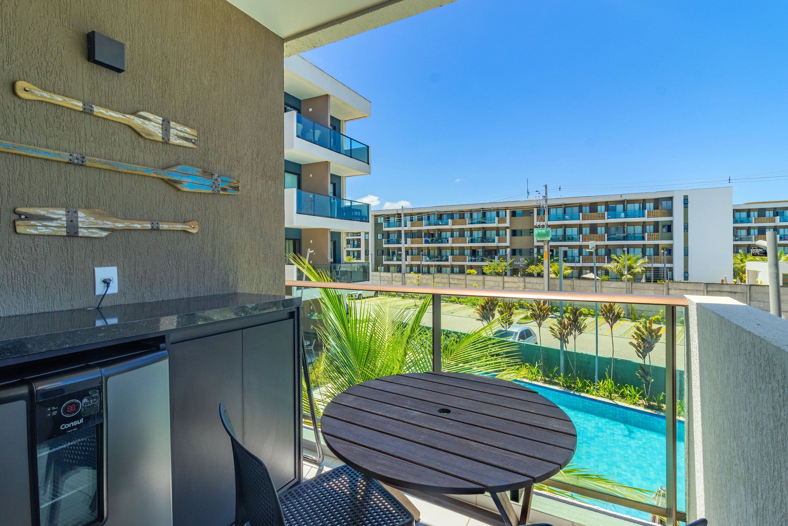 Varanda com piscina, mesa e cadeiras, com vista para um edifício moderno com várias varandas.