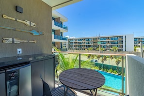 Varanda com piscina, mesa e cadeiras, com vista para um edifício moderno com várias varandas.