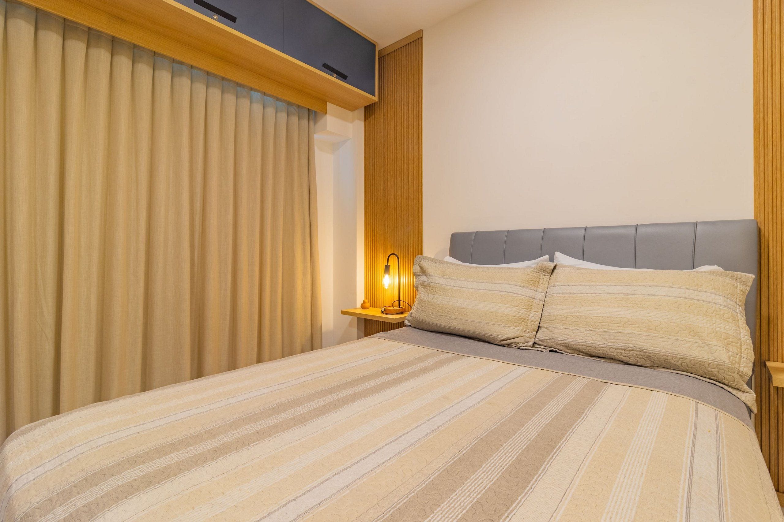 Una habitación de hotel con una cama, cortinas, una mesita de noche con lámpara y cabecero.