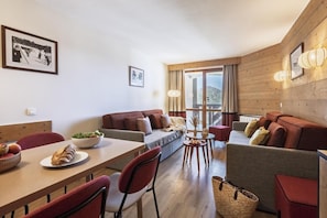 A modern living room with a sofa, dining table, and chairs. There are framed pictures on the walls and a window with curtains. - Wifi, 10m from ski slopes, balcony, ski locker, 54m², Val Thorens (Val Thorens)