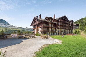 Ein mehrstöckiges Blockhaus mit Balkonen, einem Kiesplatz und Blick auf einen Berg.
