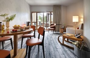 Ein Hotelzimmer mit Essbereich, einer Couch, einem Sessel, einer Lampe und Blick ins Freie.