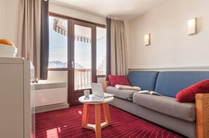 A hotel room with a sofa, a small table with a laptop, a window with curtains, and a view of mountains. - 10m from ski slopes, balcony, ski locker, 21m², Avoriaz (Avoriaz)