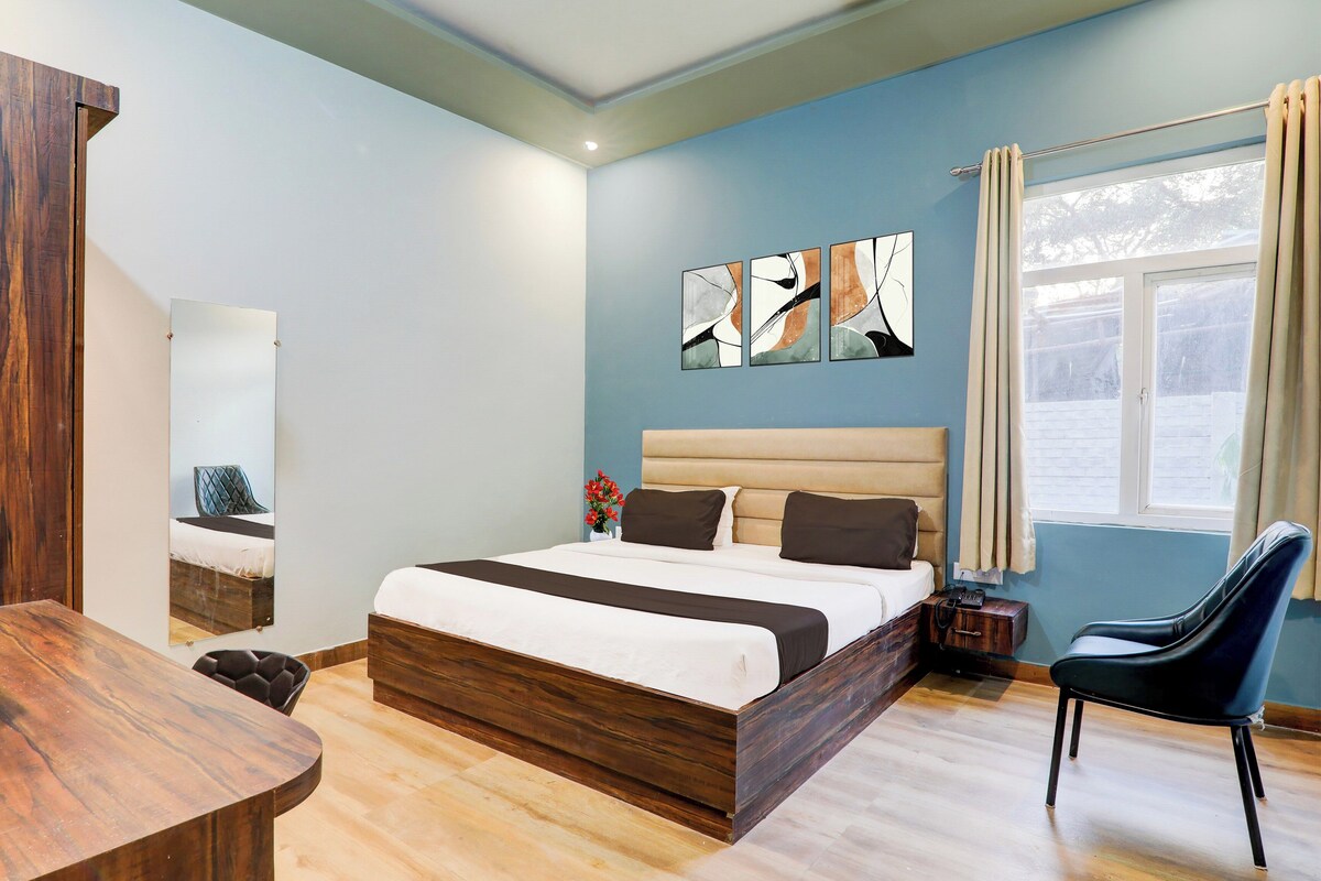 A hotel room with a bed, a chair, a wooden desk, and artwork on the wall.
