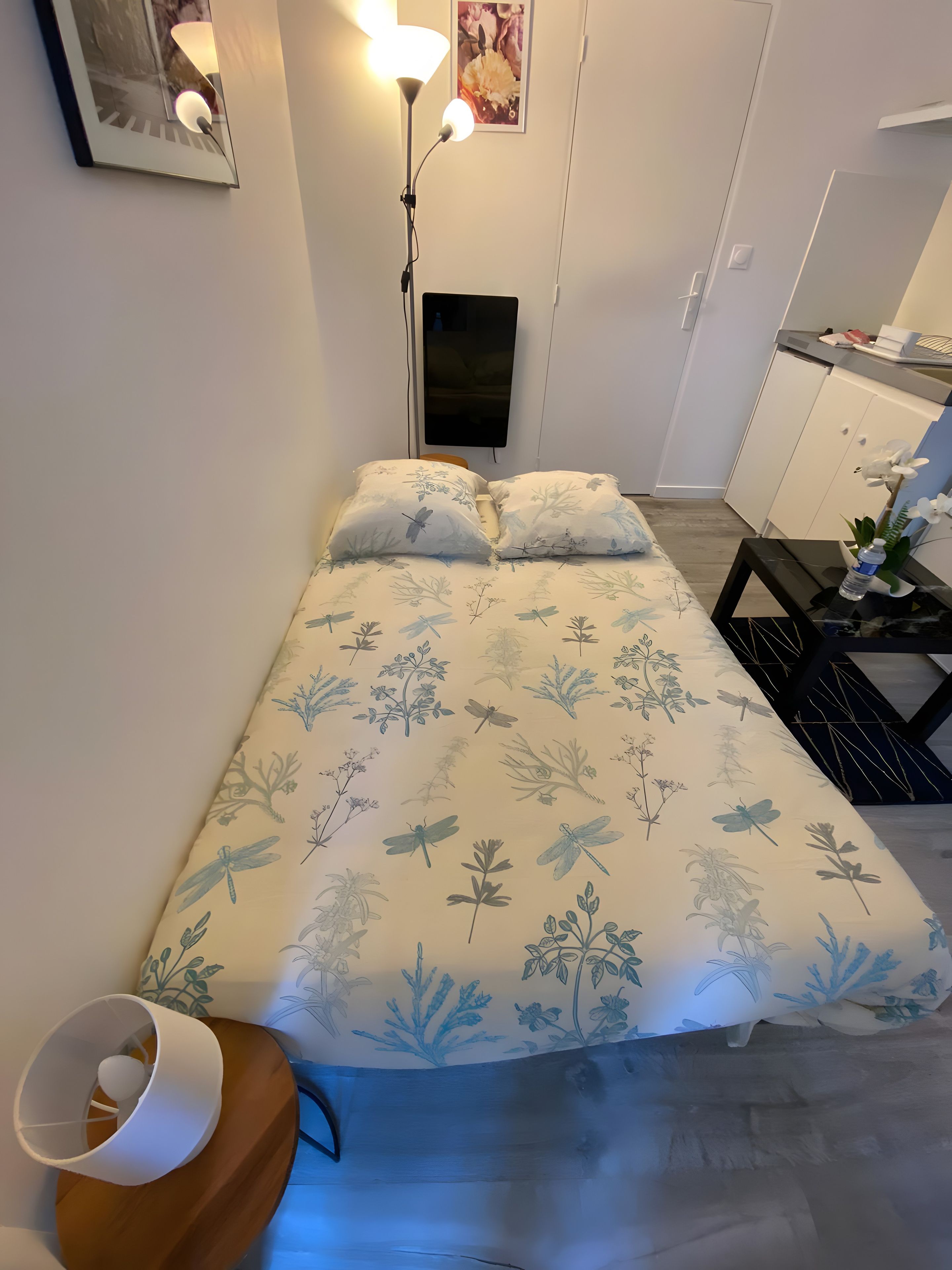 A bedroom with a bed, bedside table, lamp, and a small desk with a chair.