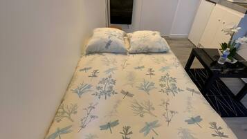 A bedroom with a bed, bedside table, lamp, and a small desk with a chair.