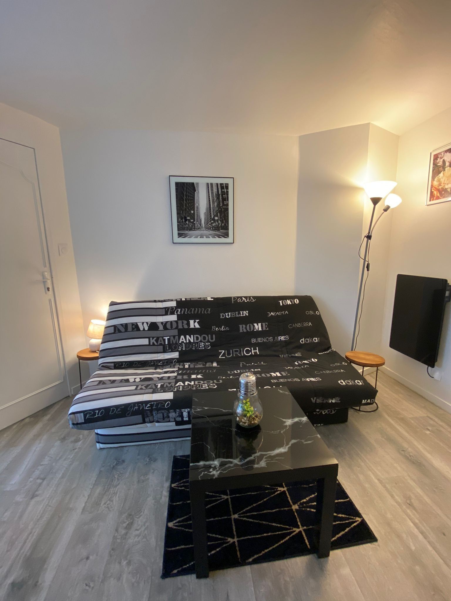 Ein modernes Schlafzimmer mit einem Bett, Nachttischen, einer Stehlampe und einem an der Wand montierten Fernseher.