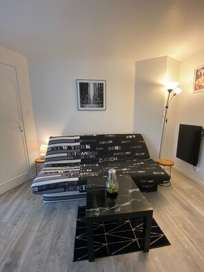 A modern bedroom with a bed, bedside tables, a floor lamp, and a wall-mounted TV. - Studio 'Studio Rouge 2 pers' (Châteaubourg)