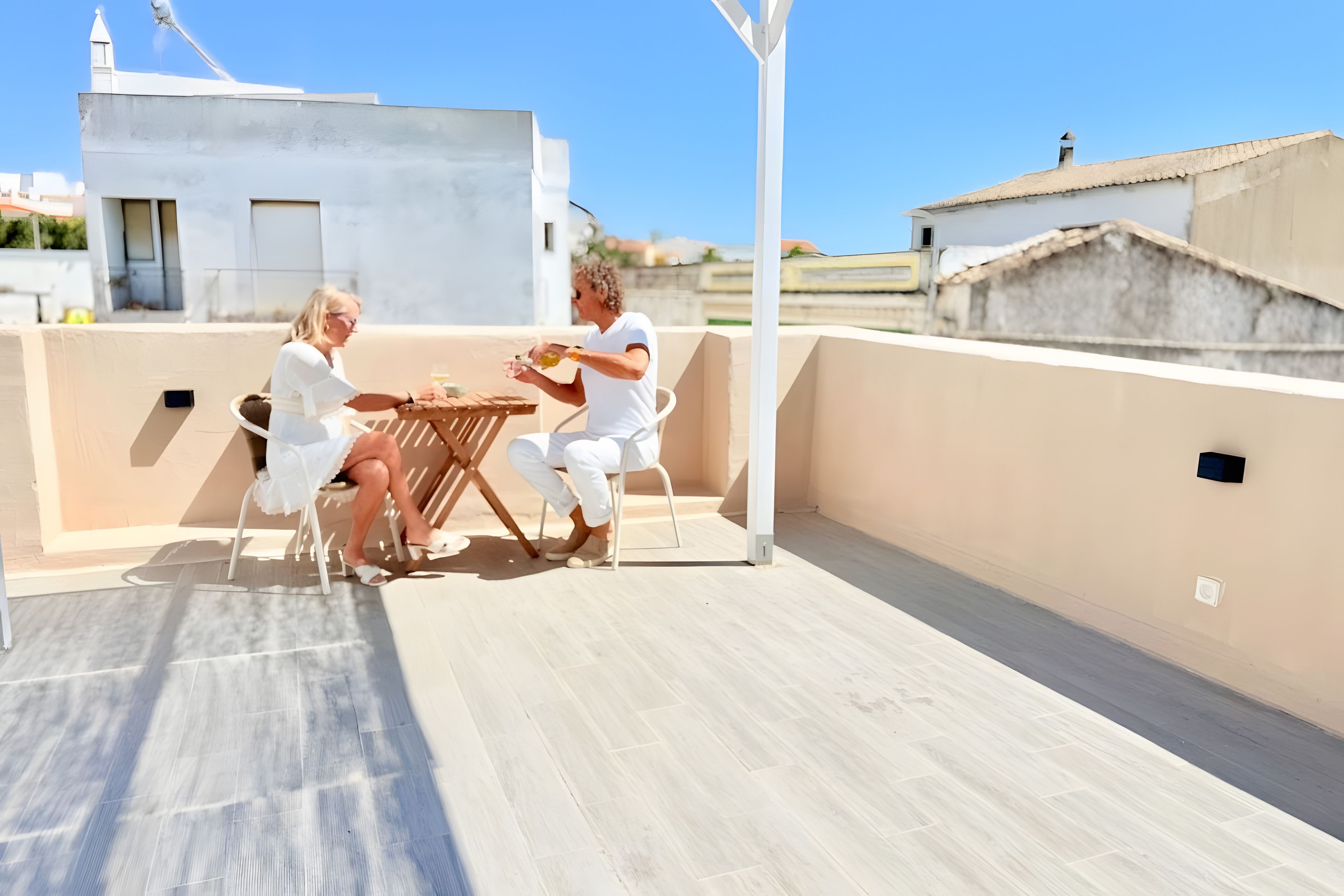 A rooftop terrace with a table and chairs, a clear sky, and buildings in the background.