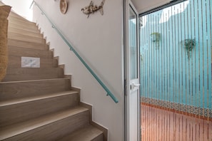 A staircase with a teal handrail leading to a glass door with a view of a balcony.