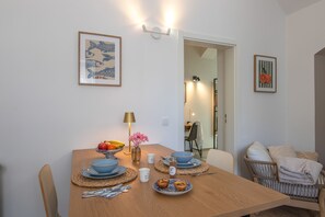 A dining area with a wooden table, plates, bowls, and cutlery. There are framed pictures on the walls and a lamp on the table.