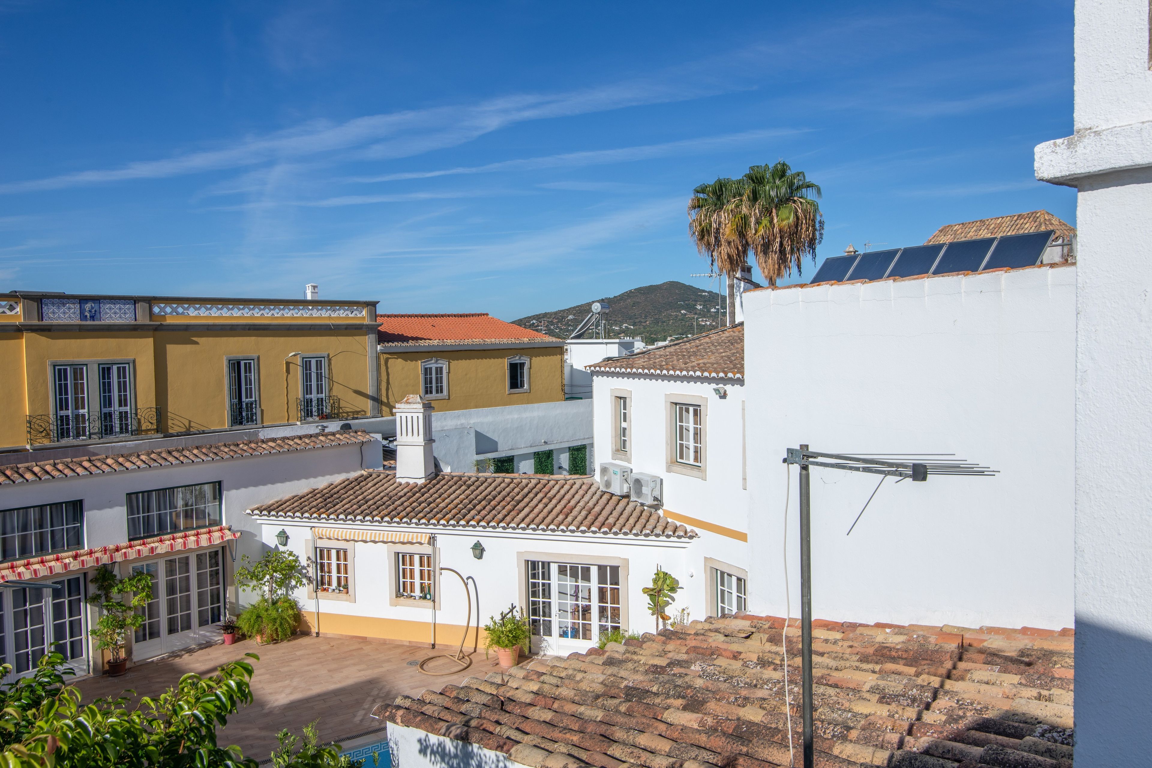 Un quartier résidentiel avec des toits recouverts de tuiles en terre cuite, un bâtiment blanc doté d’un panneau solaire et une montagne en arrière-plan.