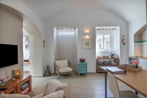 A cozy room with a television, a wicker chair, a small table with a vase, and a wooden desk.