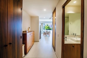 A hallway leading to a bathroom with a wooden wardrobe, a dresser, and a dining area with chairs and a table. - Paraíso MarAlma 2BR Rooftop Vista al Mar Bucerías (Bucerías)