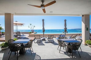 A covered outdoor seating area with tables and chairs, overlooking a pool and the sea. - Paraíso MarAlma 2BR Rooftop Vista al Mar Bucerías (Bucerías)