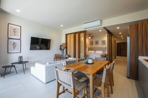 A modern living room with a dining area, a flat-screen TV mounted on the wall, and a large bed in the background. - Paraíso MarAlma 2BR Rooftop Vista al Mar Bucerías (Bucerías)