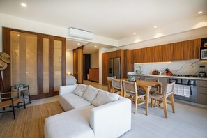 A modern living room with a sofa and dining area, a kitchen with wooden cabinets and a marble countertop, and a sliding door leading to another room. - Paraíso MarAlma 2BR Rooftop Vista al Mar Bucerías (Bucerías)
