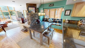 A spacious kitchen with a stone fireplace, a dining area with a long table and chairs, and a view of the outdoors through large windows. - Private Hot Tub, Pet Friendly in Frisco. Spacious Townhouse, Garage, Grill (Frisco)
