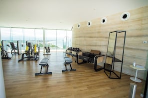A spacious gym with various exercise equipment, large windows, and a view of the city. - Best roof top Pool in Puerto Vallarta - 3 Bedroom (Nuevo Vallarta)