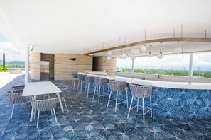 A modern outdoor bar area with a long counter, multiple bar stools, and a view of the landscape. - Best roof top Pool in Puerto Vallarta - 3 Bedroom (Nuevo Vallarta)