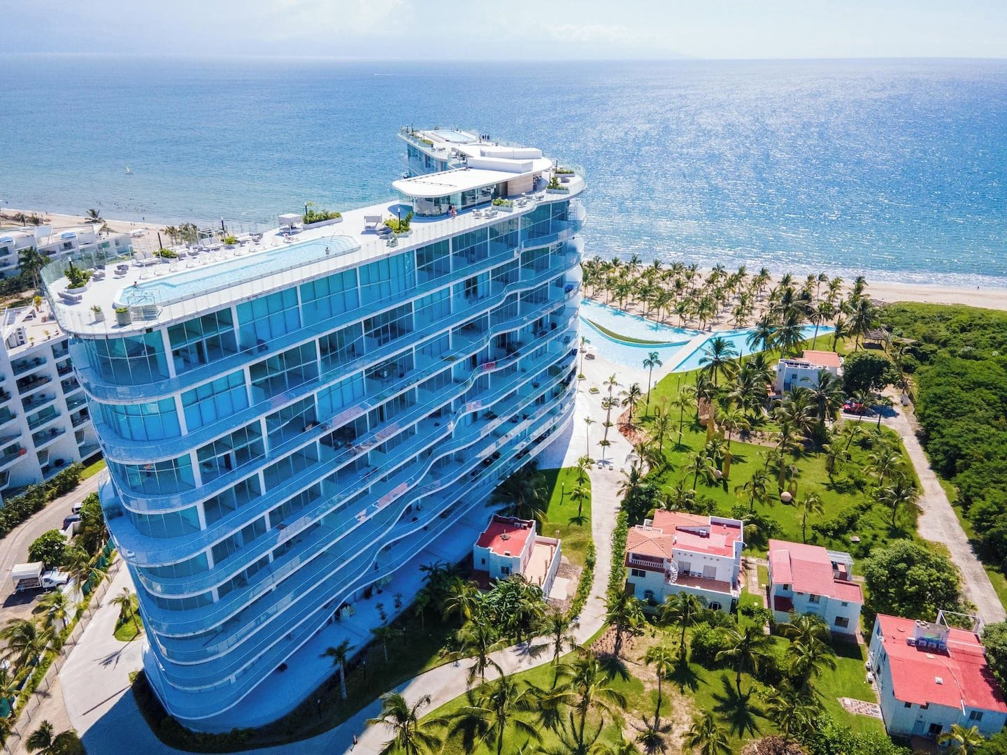 A multi-story hotel with a pool and beach view, surrounded by palm trees and a clear sky.
