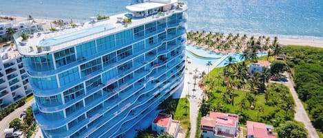 A multi-story hotel with a pool and beach view, surrounded by palm trees and a clear sky.
