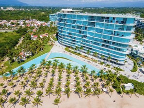 A multi-story hotel with a pool and palm trees. - Best Pool on beach and Rooftop. (Nuevo Vallarta)