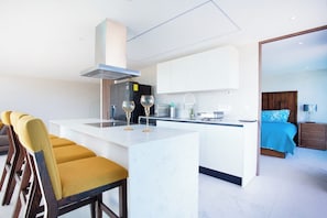 A modern kitchen with a central island, bar seating, and a bedroom with a bed and nightstand. - Best Pool on beach and Rooftop. (Nuevo Vallarta)