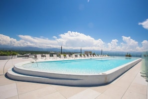 A rectangular swimming pool with a curved edge, surrounded by white lounge chairs and a glass railing. - Best Pool on beach and Rooftop. (Nuevo Vallarta)